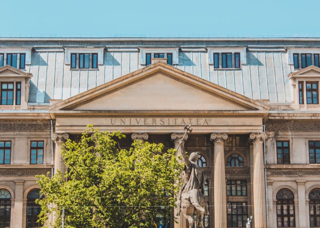 Historic university building facade with columns and greenery in daylight.