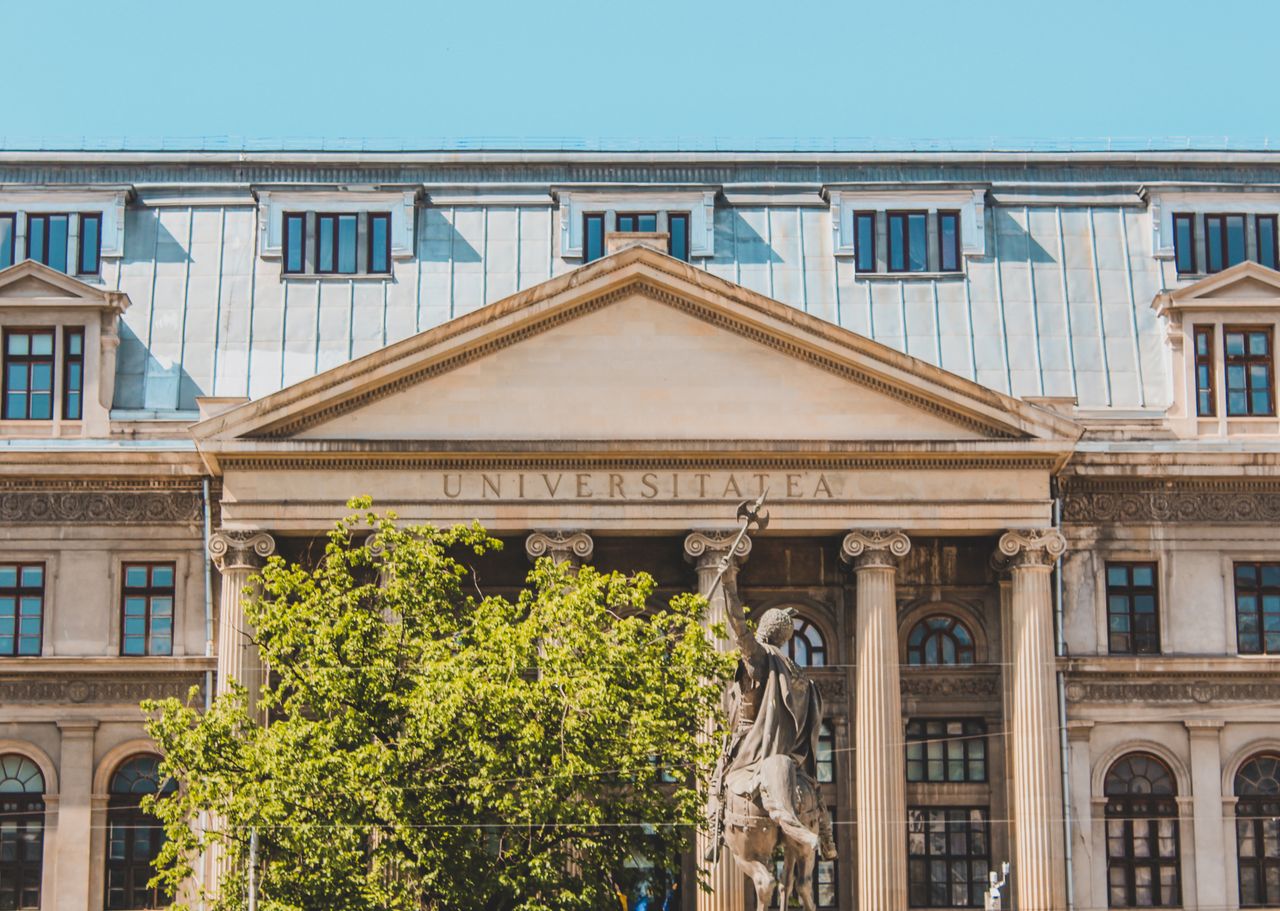 Historic university building facade with columns and greenery in daylight.
