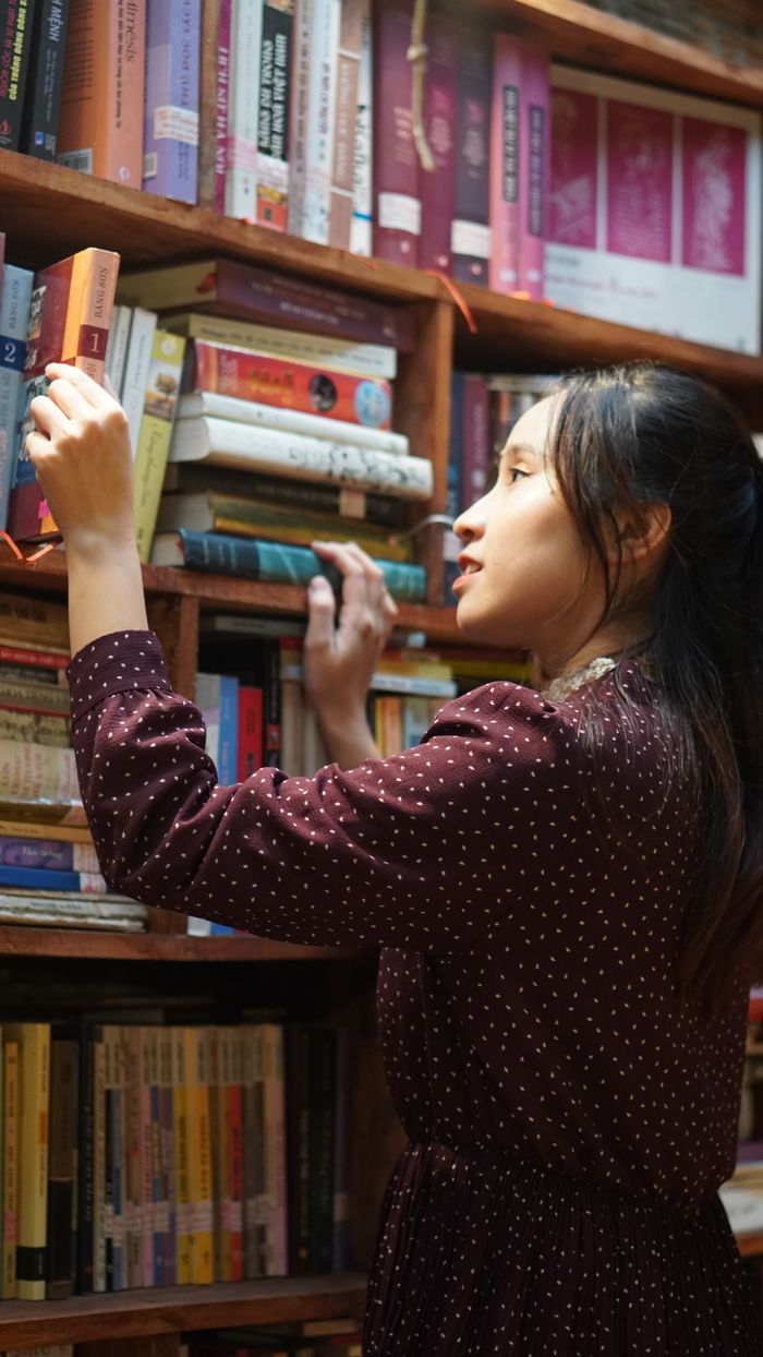 Woman in maroon dress choosing a book in a library.