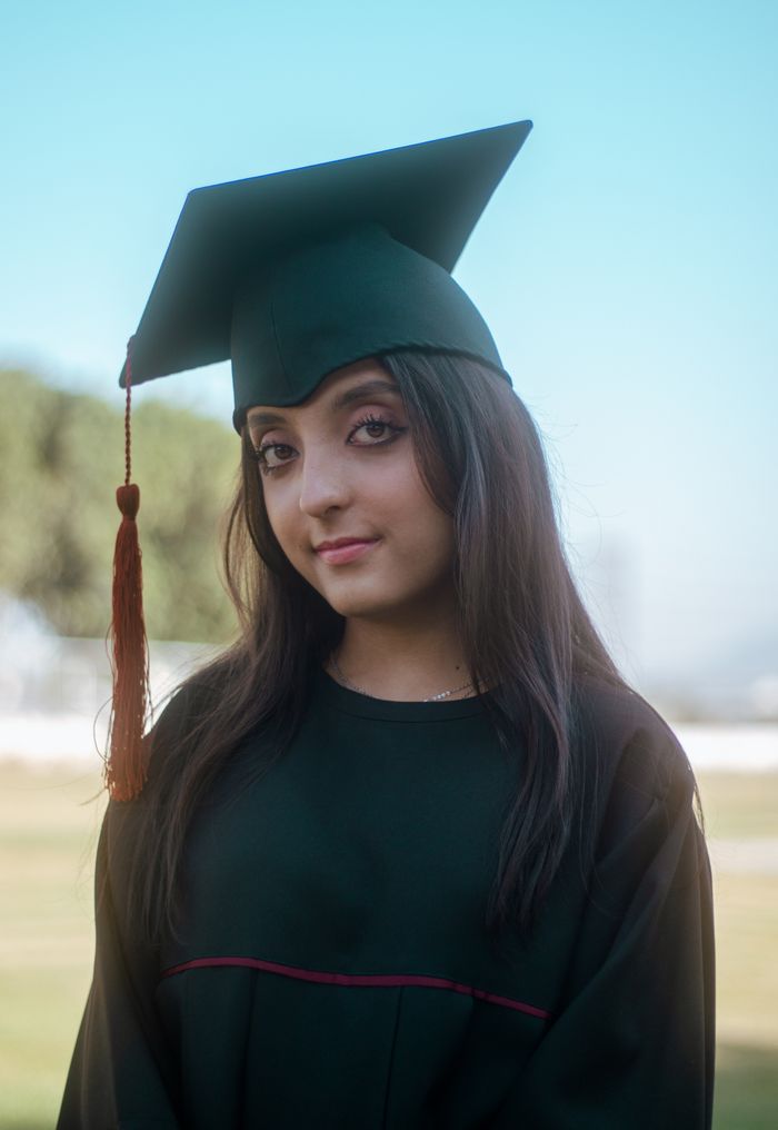 Confident young woman in graduation attire posing outdoors with a blurred background.