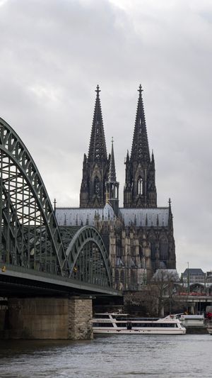 View of Cologne Cathedral and Hohenzollern Bridge over the Rhine River on a cloudy day.