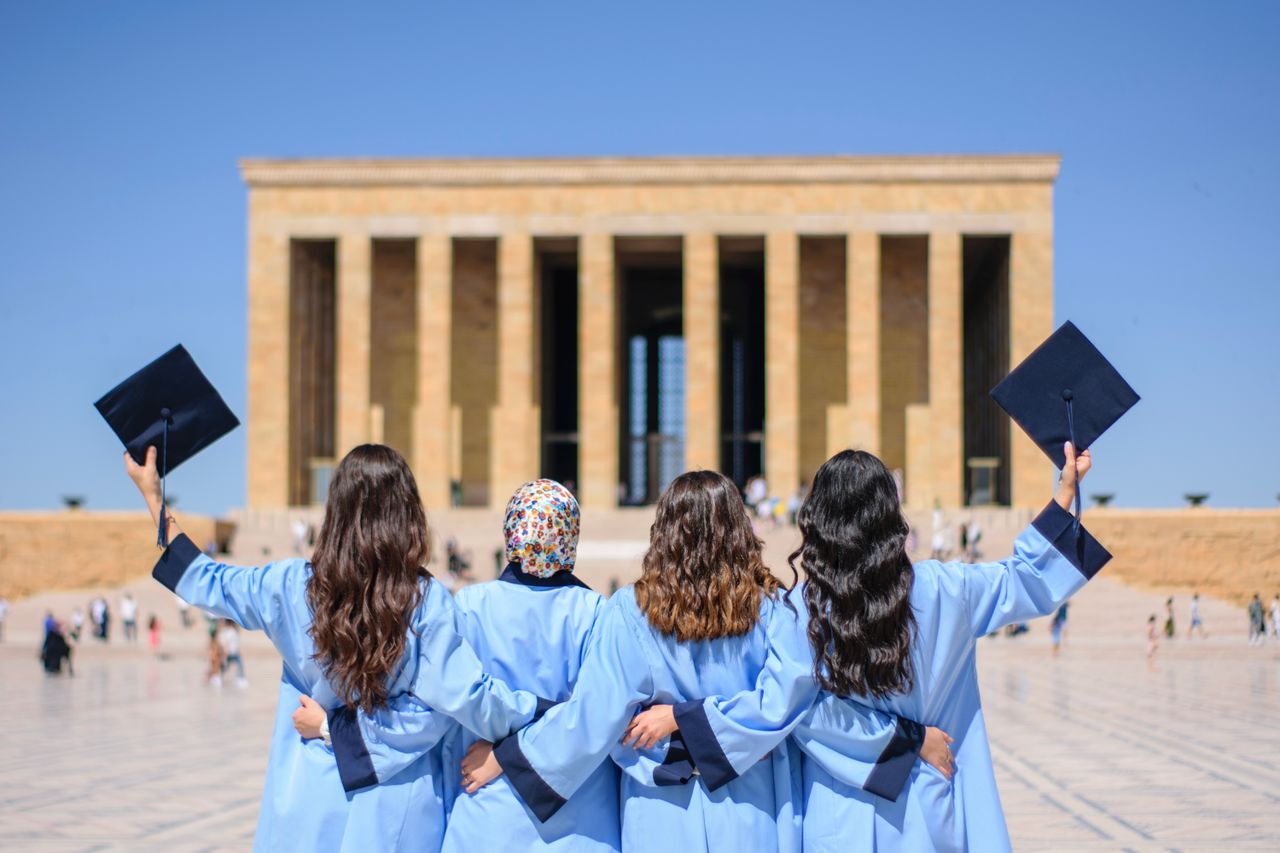 Graduates in blue gowns celebrate in front of Anıtkabir, Ankara, symbolizing academic achievement.